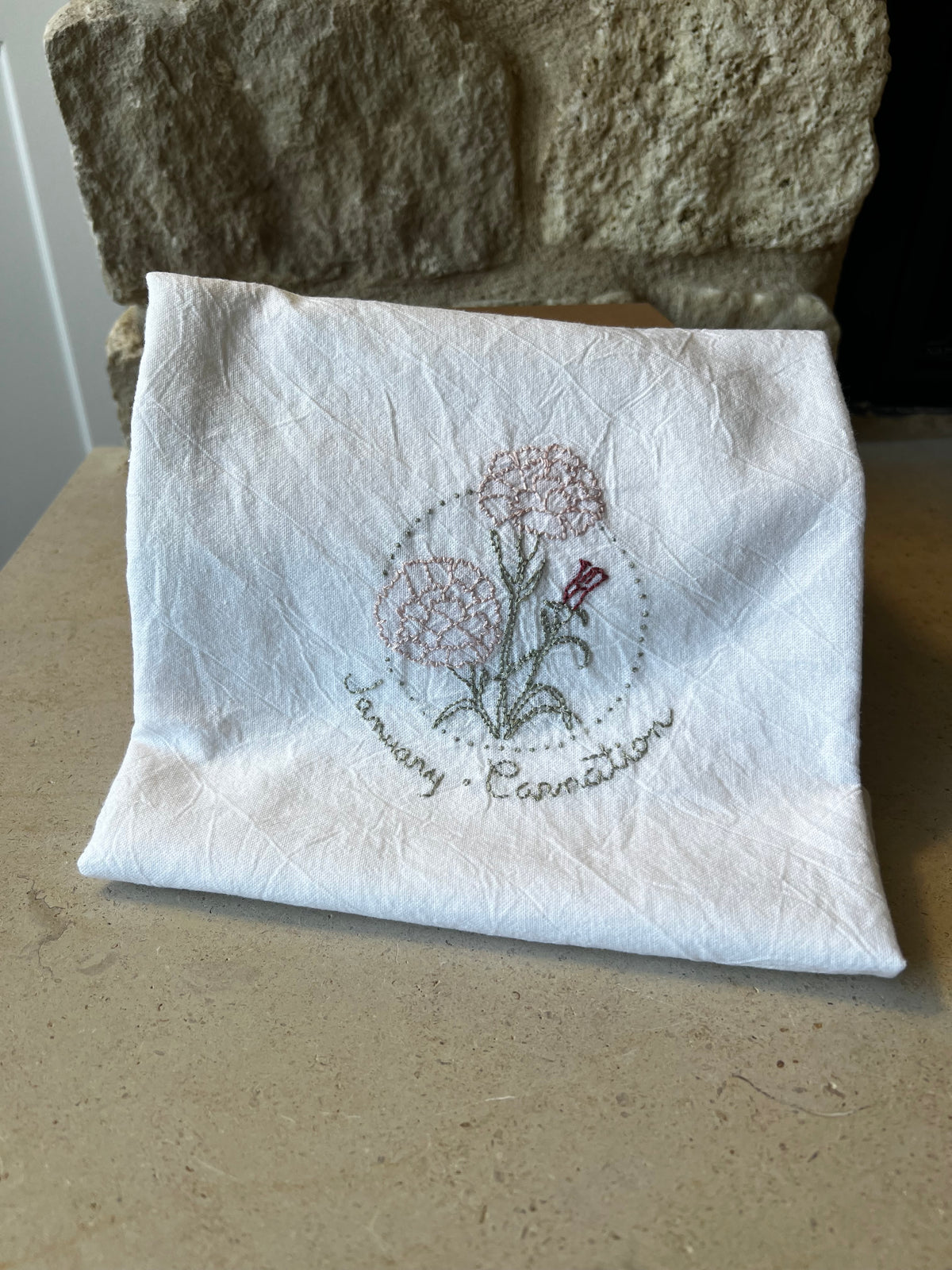 Hand-embroidered cotton tea towel, pink carnation in dotted circle, January Carnation script