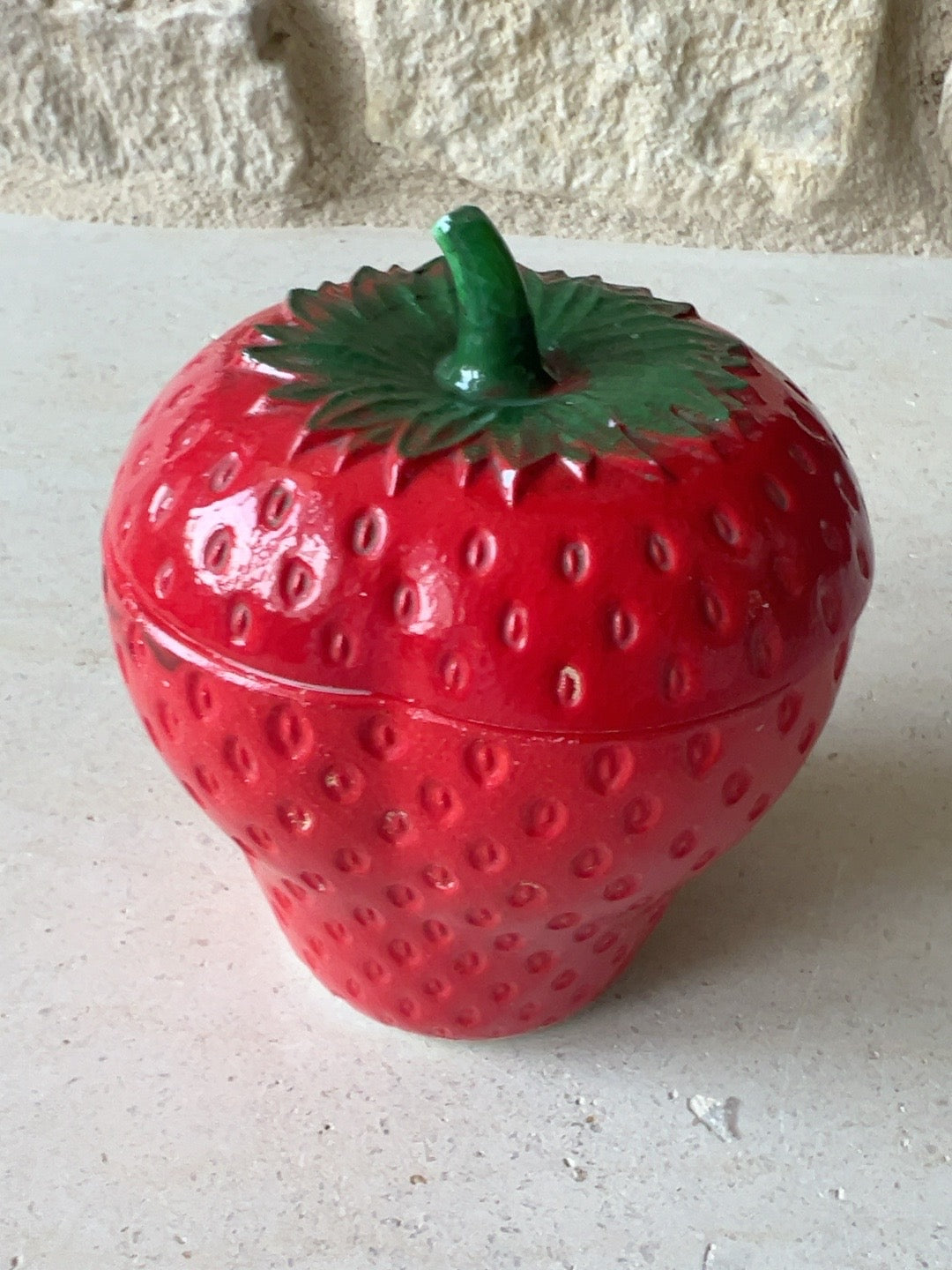 Close up of strawberry jar with green leaf lid and textured painted finish showing paint wear and surface details. 