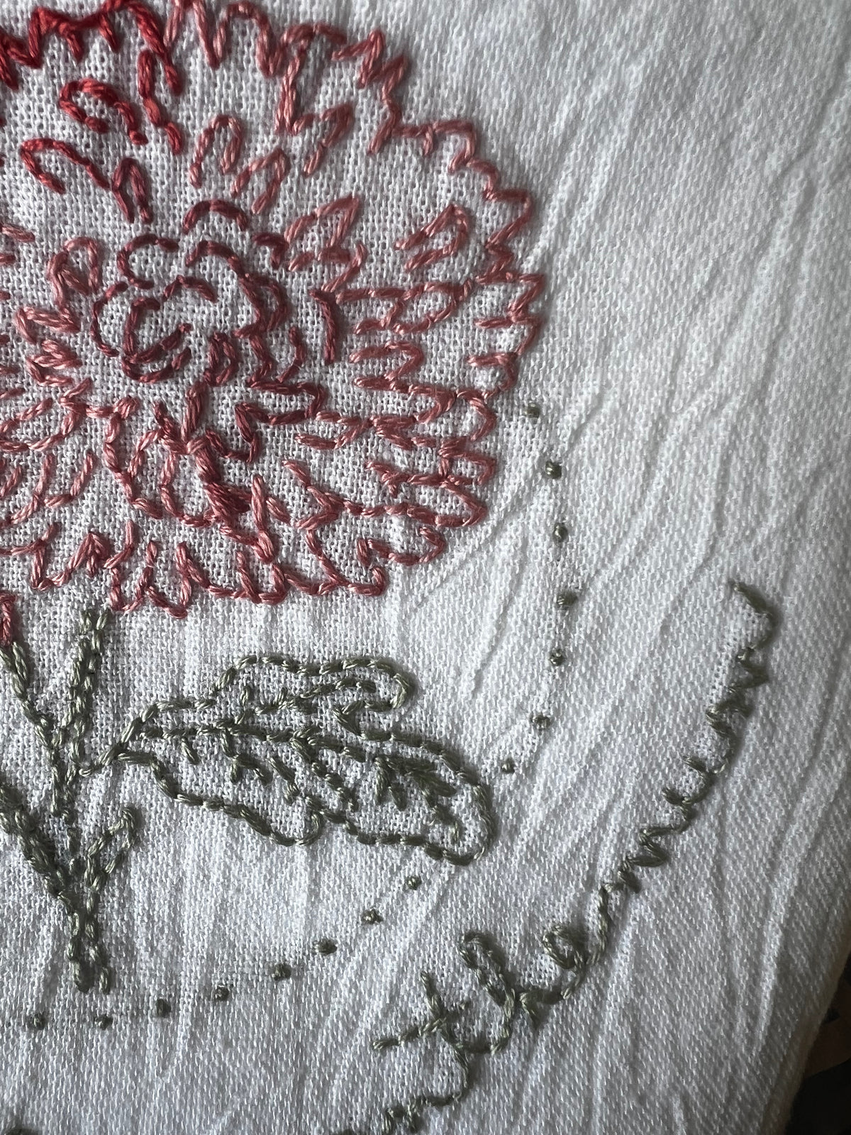 Hand-embroidered red chrysanthemum, green leaves and stem, dotted border, close-up