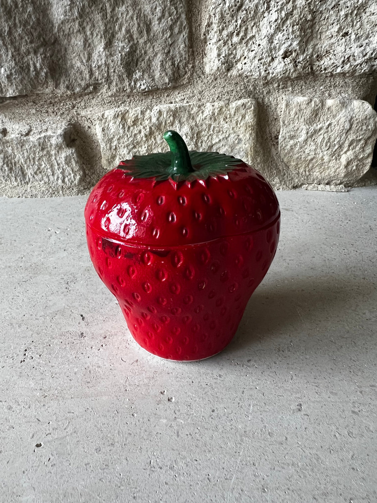 Vintage red strawberry shaped milk glass jar with textured surface and green leafy lid. 