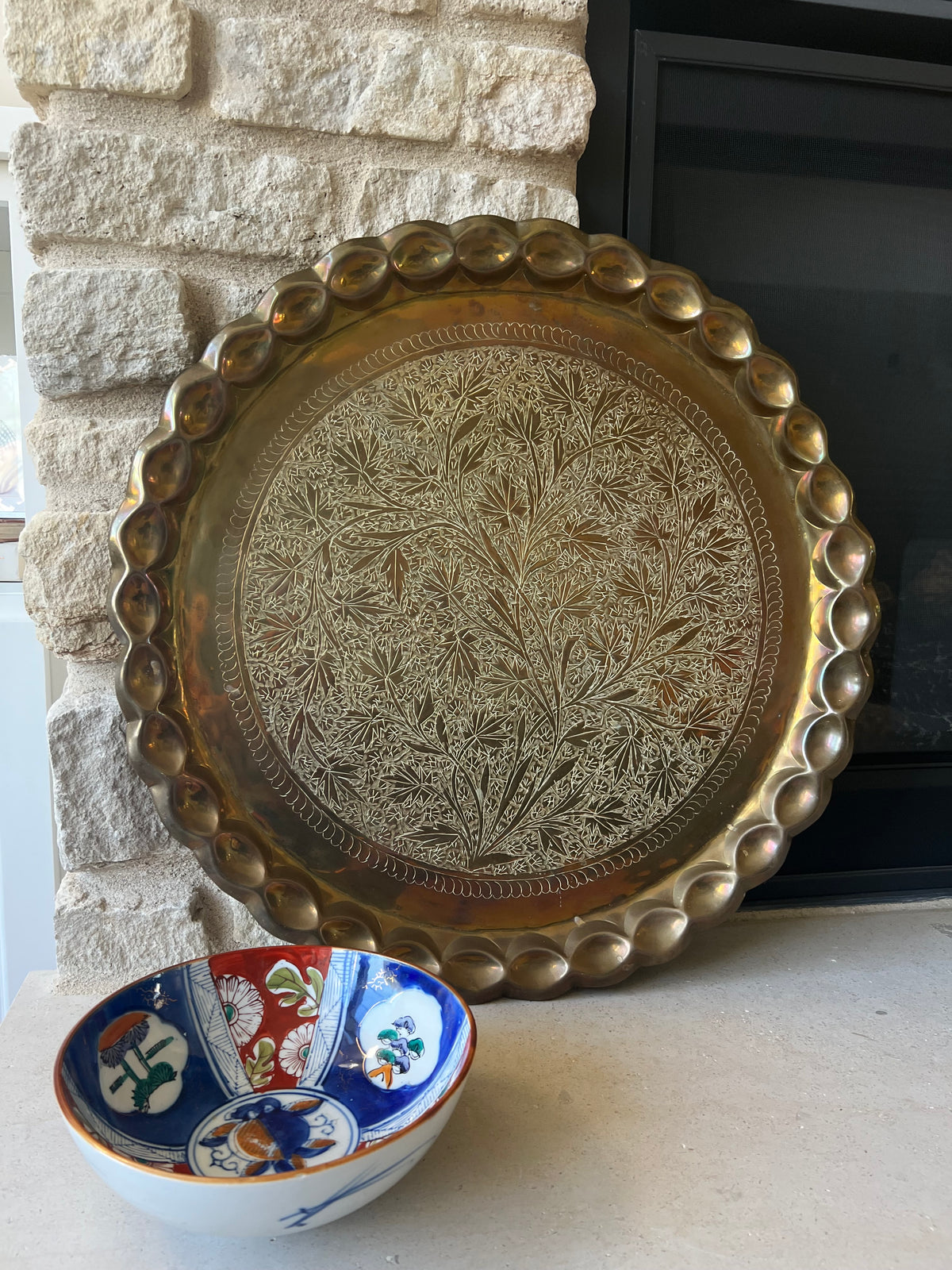 Brass tray with Imari bowl for scale, displayed against limestone fireplace.
