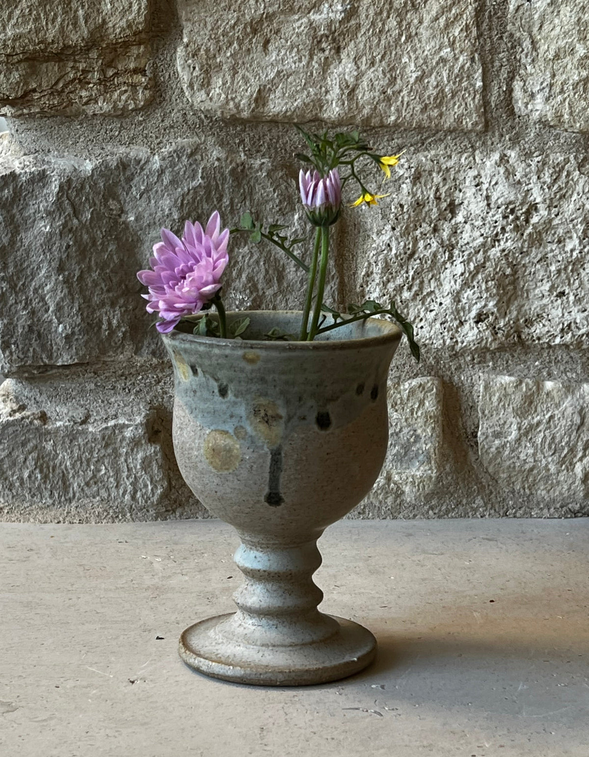 RT-stamped stoneware goblet holding pink chrysanthemum and wildflower stems, stone wall