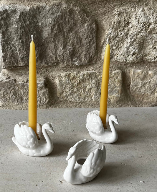 Goebel West Germany white porcelain swan taper holders, three shown, two holding yellow beeswax tapers. 
