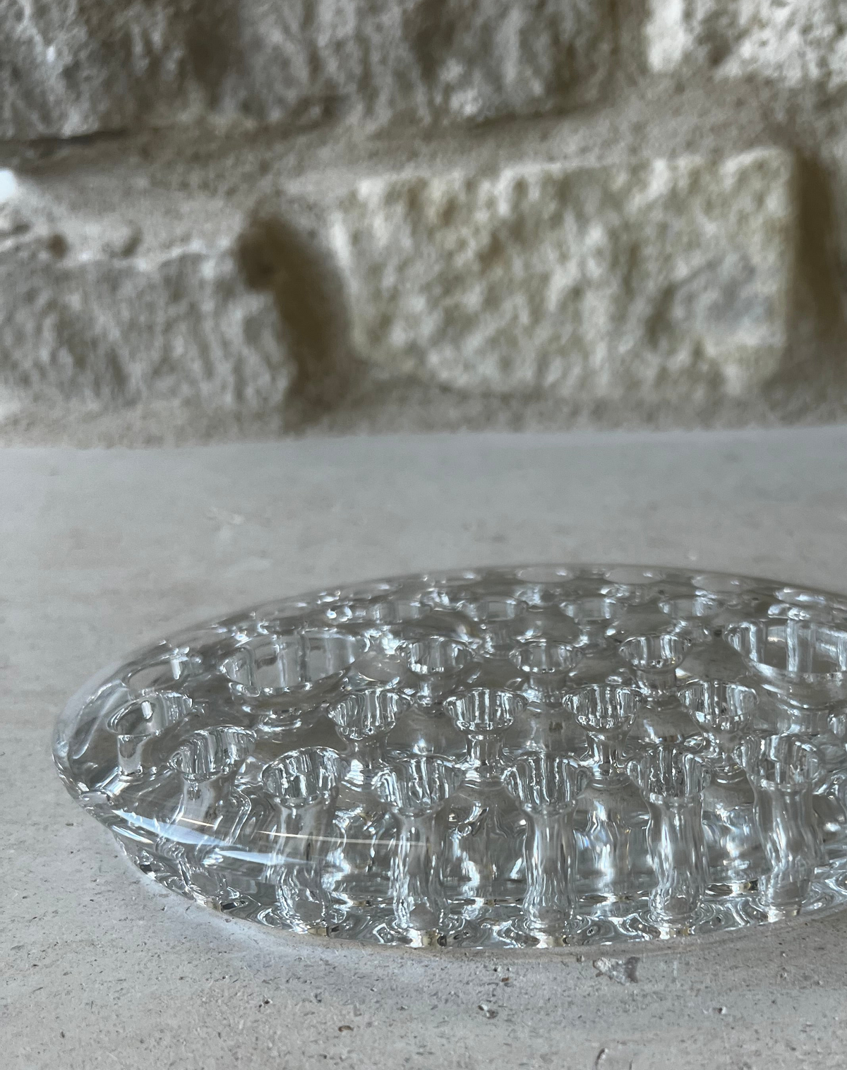 Low-profile oval clear pressed glass flower frog, side view on stone